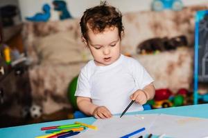 un lindo niño dibuja en su cuaderno de bocetos con lápices de colores foto