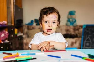 Happy little boy draws with colorful markers on a piece of paper photo