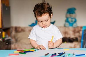 un lindo niño dibuja en su cuaderno de bocetos con lápices de colores foto