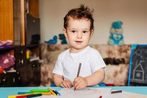un lindo niño dibuja en su cuaderno de bocetos con lápices de colores foto