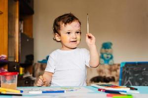 a small cute boy paints with brushes and colored paints on a sheet of paper photo