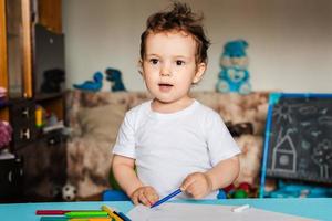 un niño pequeño dibuja en hojas de papel sobre la mesa con lápices de colores foto