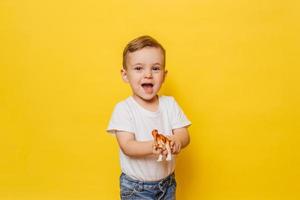 Cute laughing little boy on a yellow background with a dinosaur toy in his hands. photo