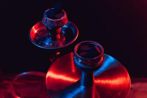 Cuenco de narguile, shisha y carbones de cerca sobre un fondo negro con iluminación de colores foto