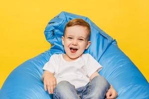 Laughing little boy on a yellow background sitting in a blue chair. photo