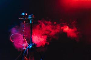 Modern hookah, shisha on a smoky black background with neon lighting and smoke. Place for your text photo