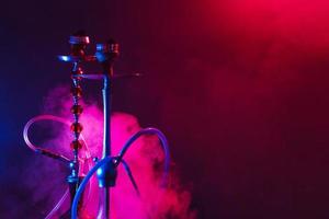 Modern hookah, shisha on a smoky black background with neon lighting and smoke. Place for your text photo