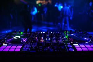 consola de dj para mezclar música con gente borrosa bailando en una fiesta de discoteca foto