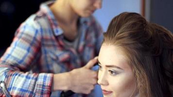 Une styliste blonde fait une coiffure à une jeune femme dans un studio de coiffure video