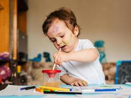 Happy cheerful child drawing with brush in album using a lot of painting tools. photo