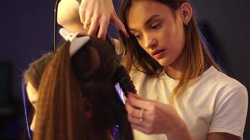 Young stylist girl makes hairstyle to a lady in hair studio video