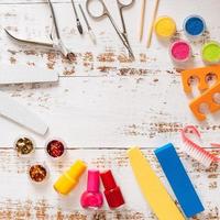 nail files, scissors, pliers, sequins and nail polishes on a white wooden background. with space for your text photo