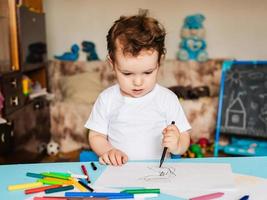un niño pequeño se sienta en una silla y dibuja con lápices de colores foto