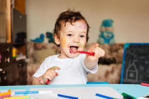 Happy little boy draws with colorful markers in an album photo