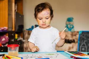 Happy cheerful child drawing with brush in album using a lot of painting tools. photo