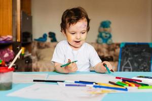 a small boy draws with colorful markers on a piece of paper photo