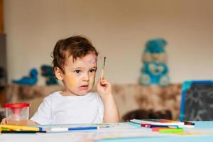 a small cute boy draws with brushes and colored paints on a sheet of paper photo