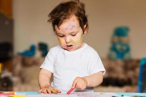 Happy little boy draws with colored pencils in an album photo