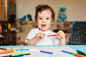 Happy little boy draws with colorful markers on a piece of paper photo