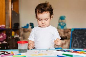 Happy cheerful child draws with a brush in an album using multi-colored paints photo