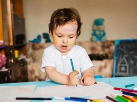 a small boy draws with colorful markers on a piece of paper photo