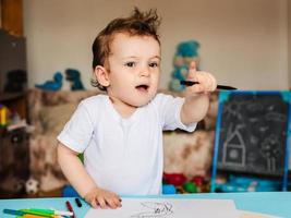 a small boy sits on a chair and draws with colored pencils photo