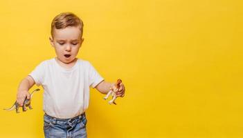 Cute laughing little boy on a yellow background with a dinosaur toy in his hands. Copy space. photo