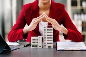 Female real estate agent is use hands to protect red roof for the concept of real estate investment about house trading, purchase at desk in office photo