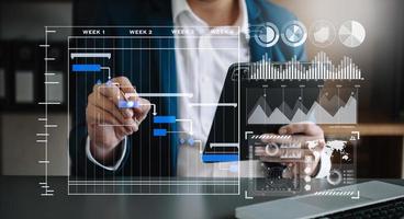 Businessman hand Project manager working and update tasks and Gantt chart scheduling virtual diagram.with smart phone, tablet and laptop photo