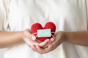 mano de mujer sosteniendo un corazón rojo con una máscara protectora foto