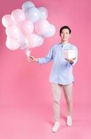 Young Asian man holding balloon on pink background photo