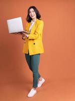 Full length photo of young Asian woman using laptop on background