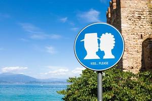 Kiss street sign located in public area in front of Sirmione castle, Italy. Concept of love, couple, romantic. photo