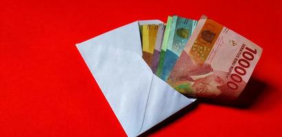 Indonesian Rupiah in white envelope isolated on red background. The concept of giving angpao on Chinese New Year photo