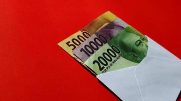 Indonesian Rupiah 5000, 10000 and 20000 in white envelope isolated on red background photo