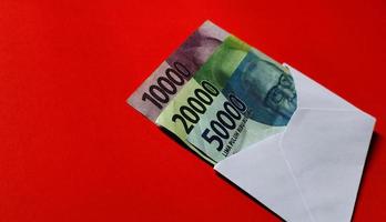 Indonesian Rupiah 10.000, 20.000 and 50.000 in white envelope isolated on red background photo