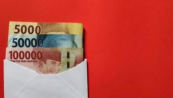 Indonesian rupiah nominal 5000, 50000 and 100000 rupiah in white envelope isolated on red background. photo