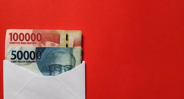 Indonesian rupiah nominal 50000 and 100000 rupiah in white envelope isolated on red background. photo