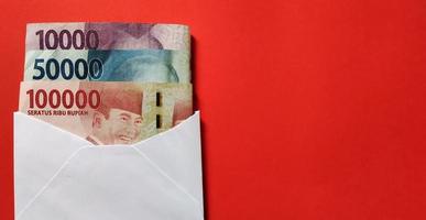 Indonesian Rupiah in white envelope isolated on red background. The concept of giving angpao photo