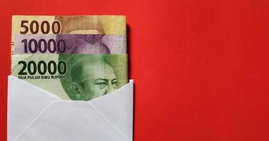 Indonesian rupiah in a white envelope isolated on red background. Free space photo