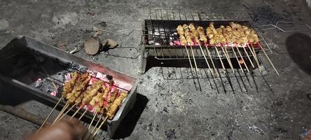 A few skewers of raw, seasoned chicken skewers and being grilled, ready to be served photo