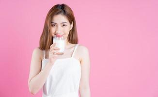 Image of young Asian woman drinking milk on pink background photo
