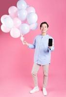 Young Asian man holding balloon on pink background photo