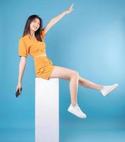 Full length photo of young Asian woman using smartphone on blue background
