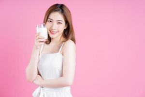 Image of young Asian woman drinking milk on pink background photo