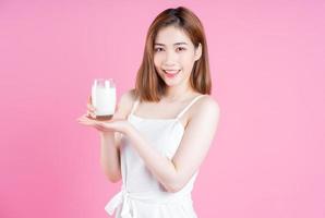 Image of young Asian woman drinking milk on pink background photo