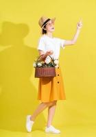 Full length photo of young Asian woman holding flower on yellow background