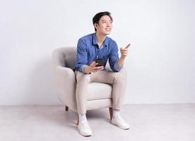 joven asiático sentado en un sillón de fondo blanco foto