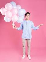 Young Asian man holding balloon on pink background photo