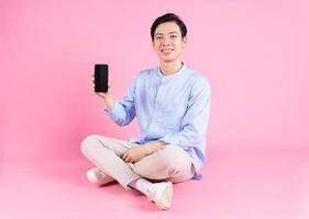 joven asiático sentado y usando un teléfono inteligente en el fondo foto